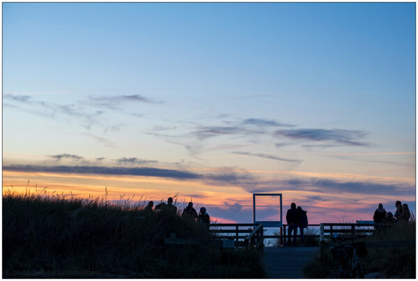 Mehrer Personen stehen in Kampen/Sylt auf dem Roten Kliff und blicken aufs Meer in den Sonnenuntergang